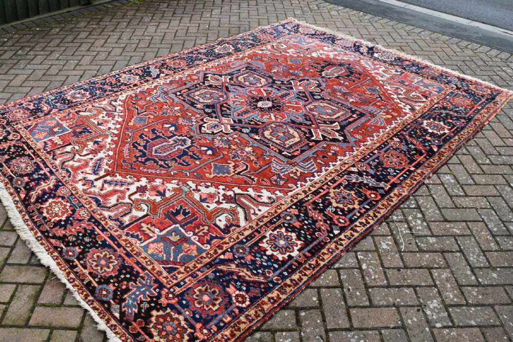 An antique Persian Heriz hand-knotted wool rug featuring a large geometric central medallion in navy blue, rust red, and cream tones. View IV