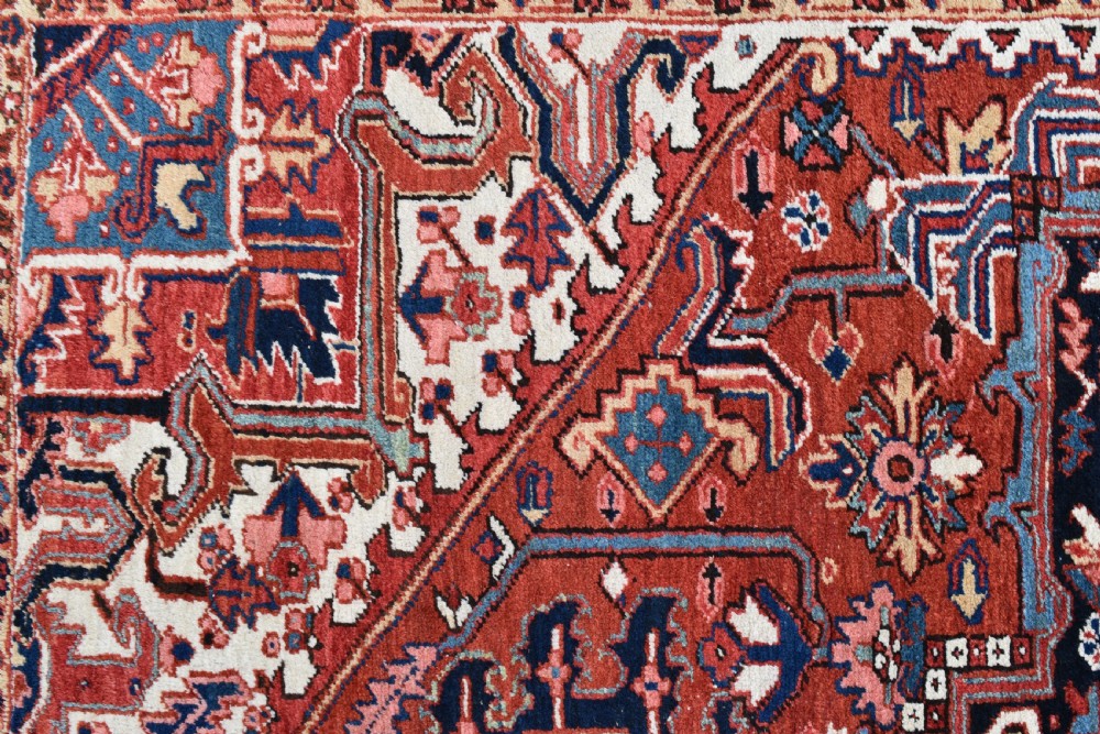 An antique Persian Heriz hand-knotted wool rug featuring a large geometric central medallion in navy blue, rust red, and cream tones. View V
