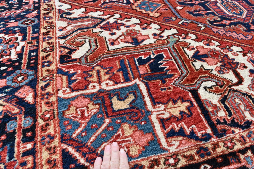 An antique Persian Heriz hand-knotted wool rug featuring a large geometric central medallion in navy blue, rust red, and cream tones. View VI