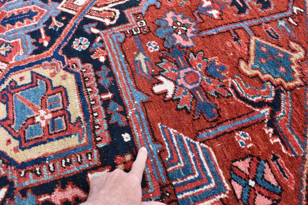 An antique Persian Heriz hand-knotted wool rug featuring a large geometric central medallion in navy blue, rust red, and cream tones. View VII