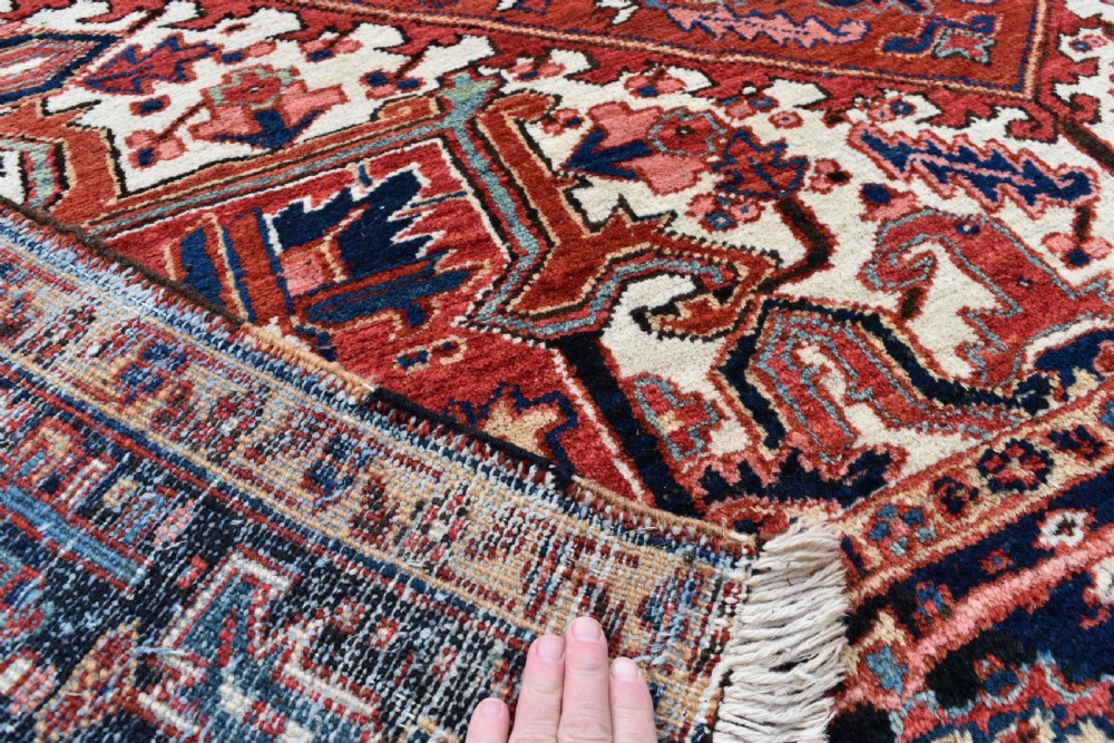 An antique Persian Heriz hand-knotted wool rug featuring a large geometric central medallion in navy blue, rust red, and cream tones. View VIII