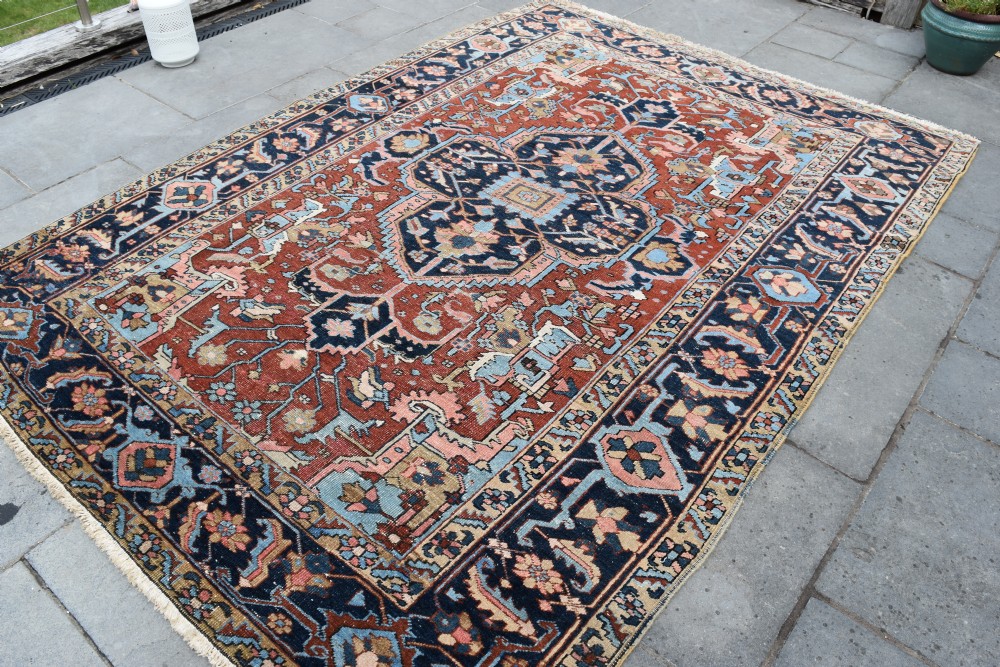 An antique hand-knotted Persian Heriz carpet featuring a large geometric central medallion in navy blue, light blue, and terracotta surrounded by ornate botanical borders.