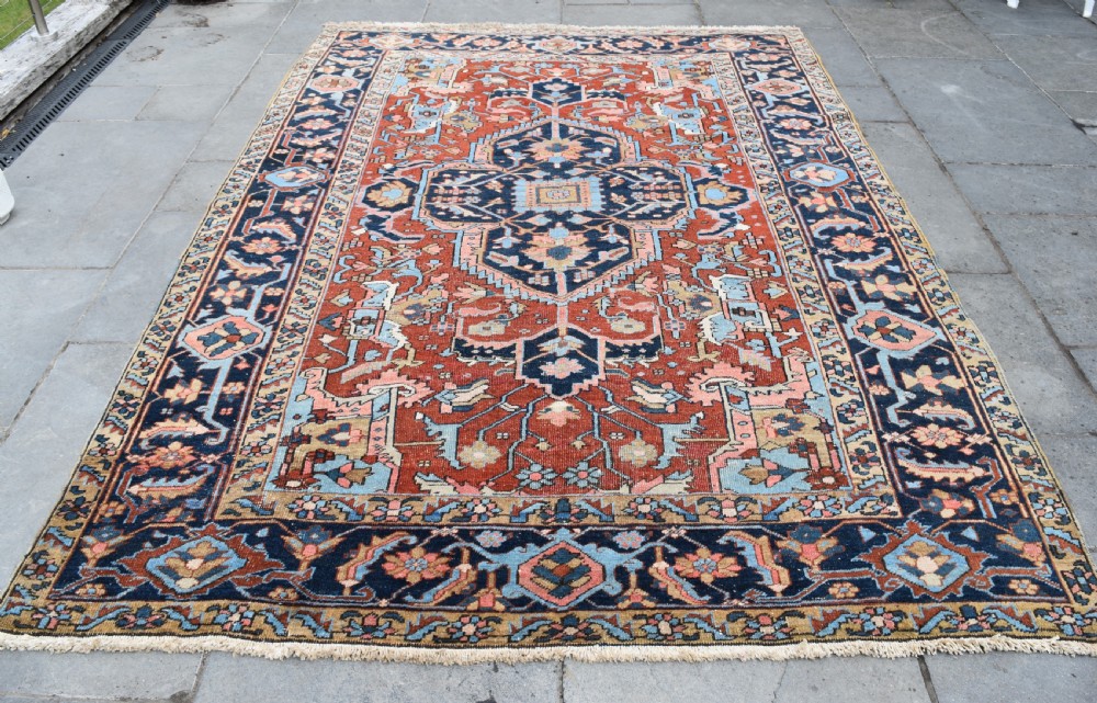 An antique hand-knotted Persian Heriz carpet featuring a large geometric central medallion in navy blue, light blue, and terracotta surrounded by ornate botanical borders. View III
