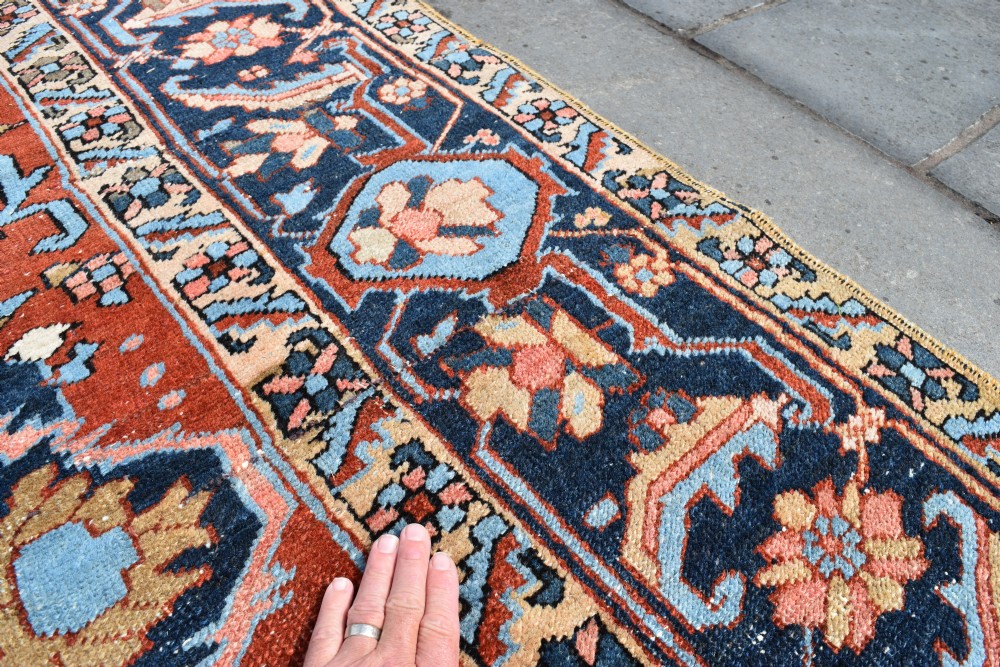 An antique hand-knotted Persian Heriz carpet featuring a large geometric central medallion in navy blue, light blue, and terracotta surrounded by ornate botanical borders. View V