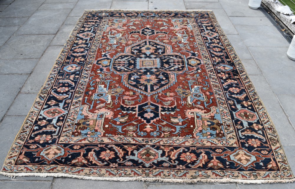 An antique hand-knotted Persian Heriz carpet featuring a large geometric central medallion in navy blue, light blue, and terracotta surrounded by ornate botanical borders. View VI