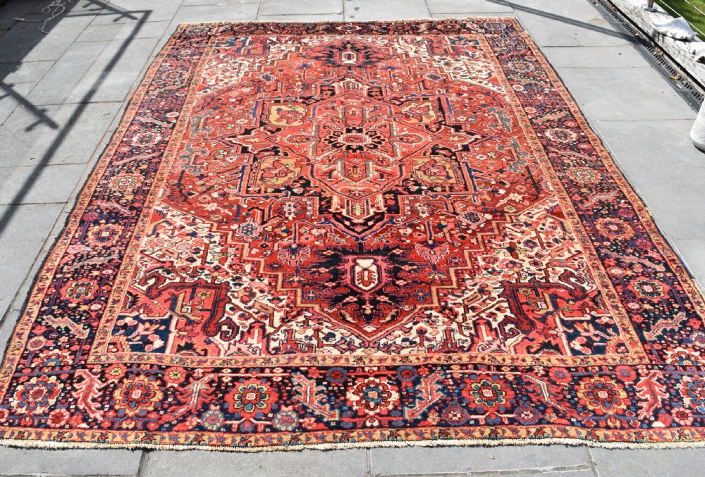 An antique hand-knotted Heriz wool rug featuring a large geometric central medallion in navy and ivory surrounded by a terracotta red field and patterned borders. View II