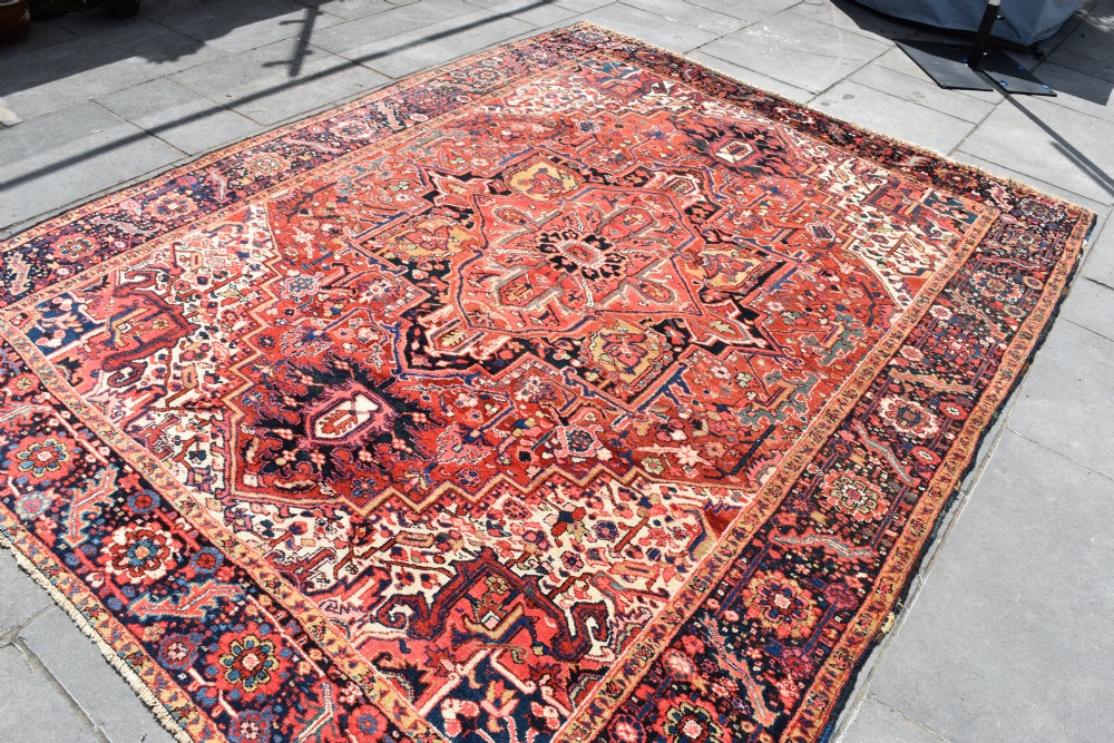 An antique hand-knotted Heriz wool rug featuring a large geometric central medallion in navy and ivory surrounded by a terracotta red field and patterned borders. View III