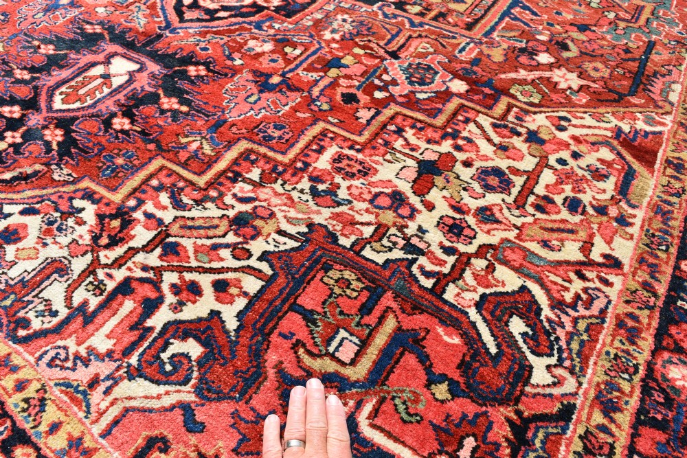 An antique hand-knotted Heriz wool rug featuring a large geometric central medallion in navy and ivory surrounded by a terracotta red field and patterned borders. View V