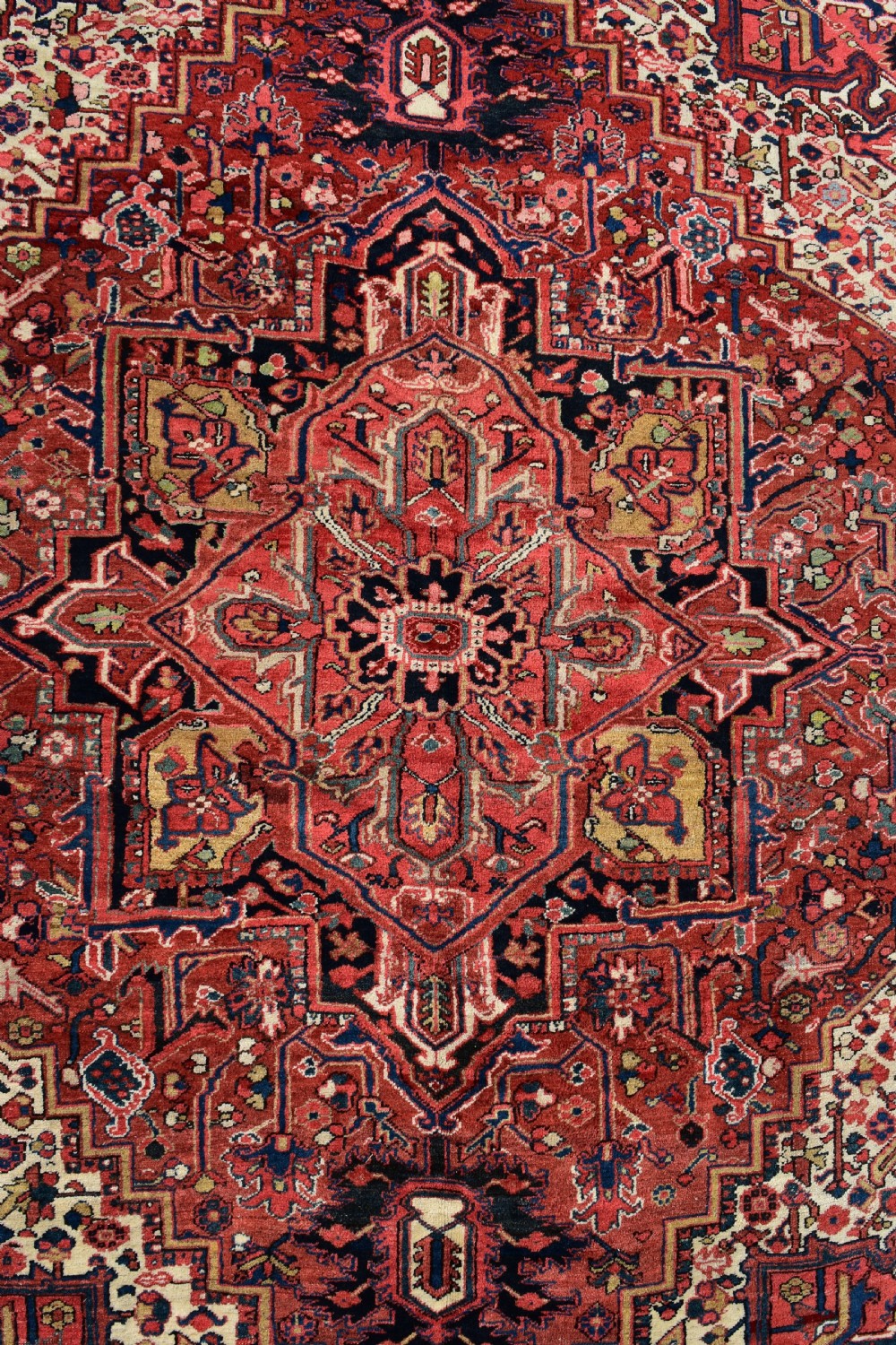 An antique hand-knotted Heriz wool rug featuring a large geometric central medallion in navy and ivory surrounded by a terracotta red field and patterned borders. View VII