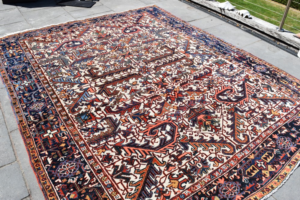 A large antique hand-knotted Heriz wool carpet featuring an allover cream field decorated with intricate geometric floral motifs and framed by a dark navy patterned border.