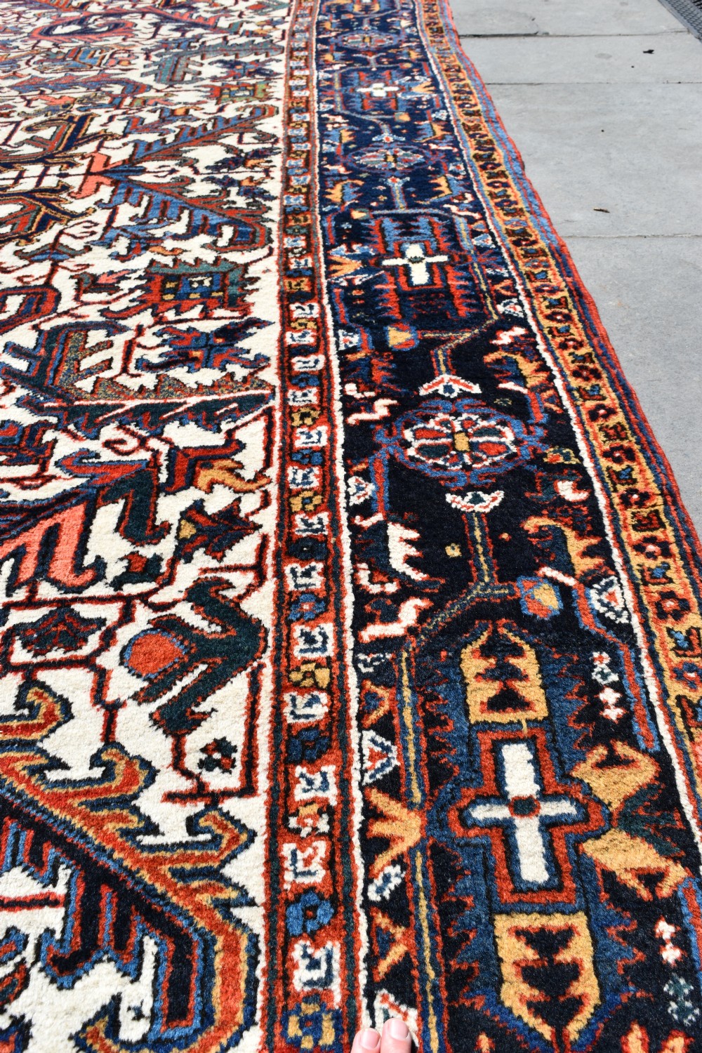 A large antique hand-knotted Heriz wool carpet featuring an allover cream field decorated with intricate geometric floral motifs and framed by a dark navy patterned border. View IV