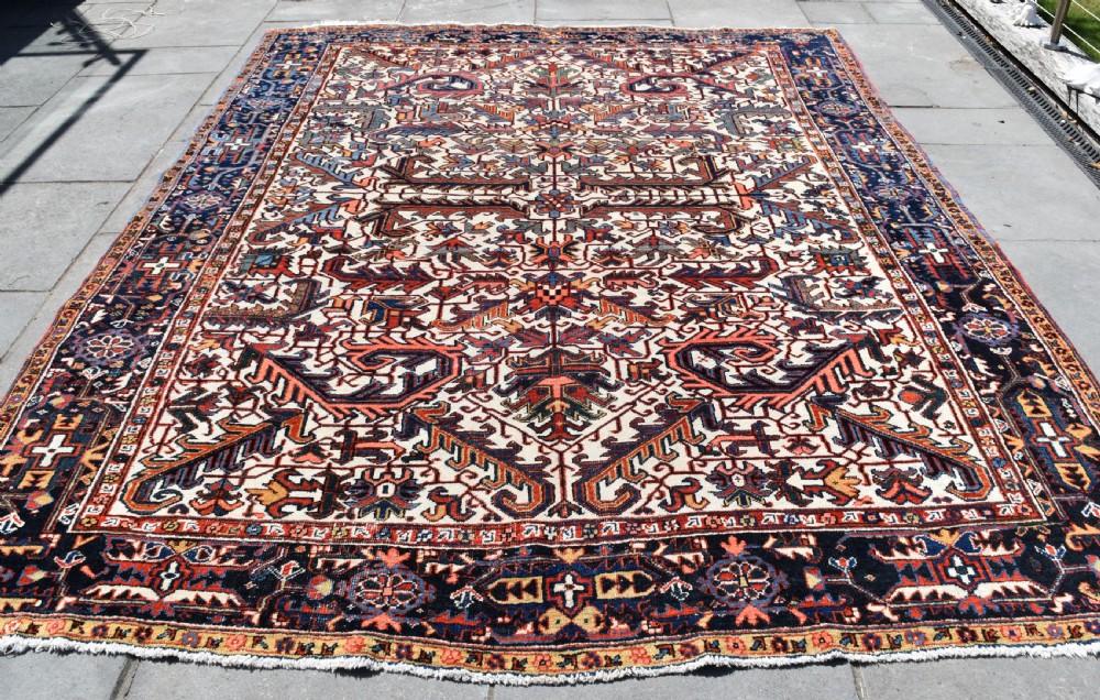 A large antique hand-knotted Heriz wool carpet featuring an allover cream field decorated with intricate geometric floral motifs and framed by a dark navy patterned border. View V