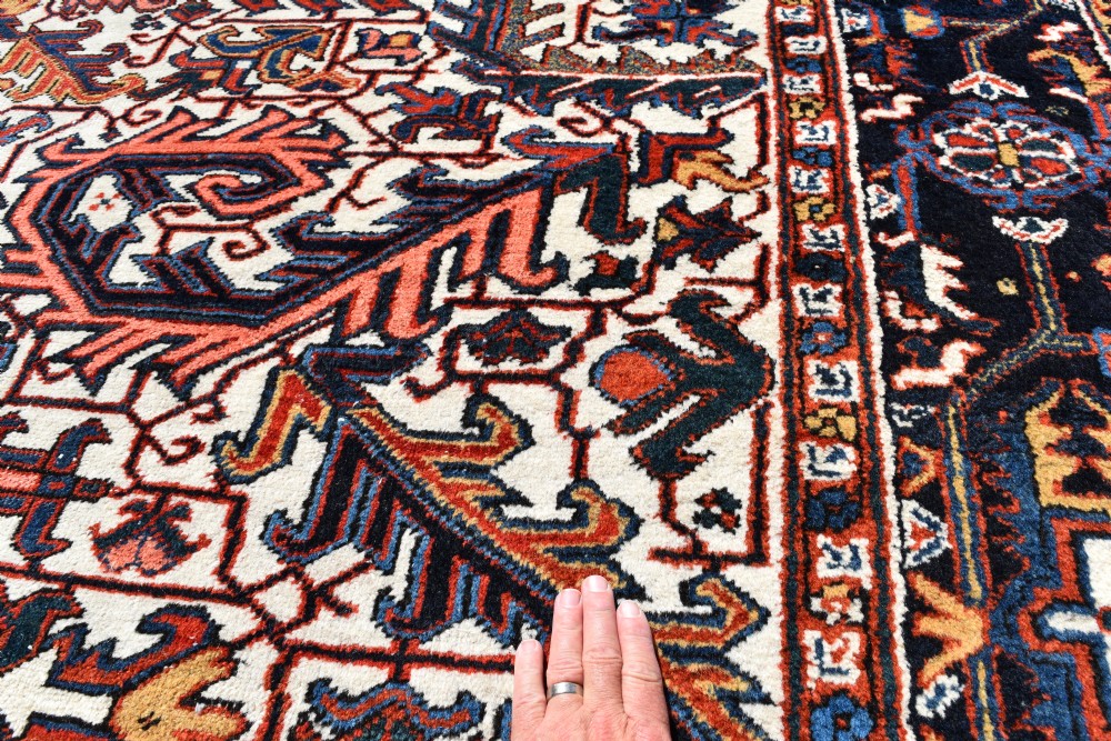A large antique hand-knotted Heriz wool carpet featuring an allover cream field decorated with intricate geometric floral motifs and framed by a dark navy patterned border. View VI