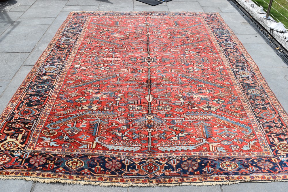 A large hand-knotted Persian Heriz carpet displaying a dense geometric all-over motif in terracotta red, sky blue, and navy blue.