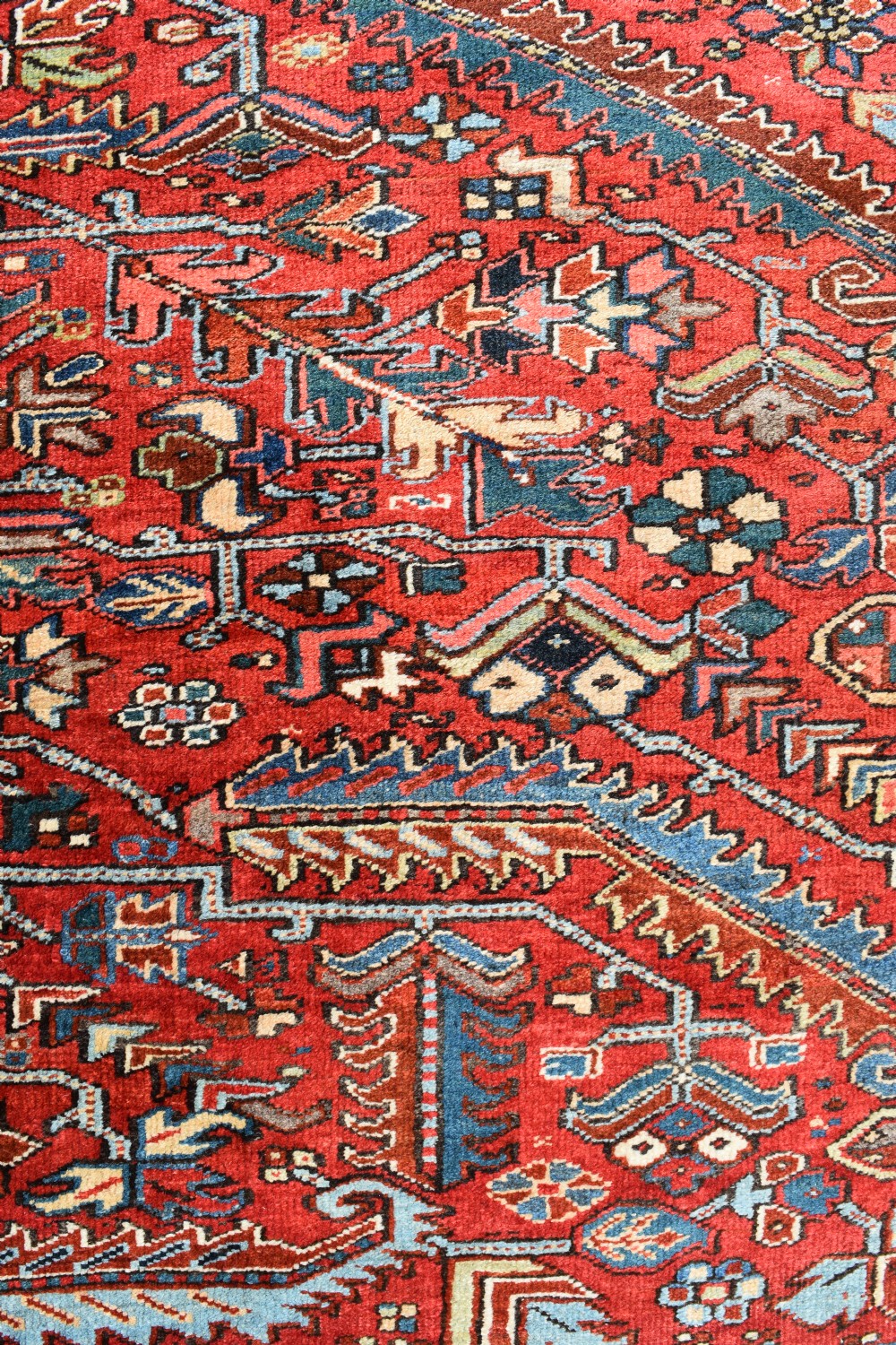 A large hand-knotted Persian Heriz carpet displaying a dense geometric all-over motif in terracotta red, sky blue, and navy blue. View V