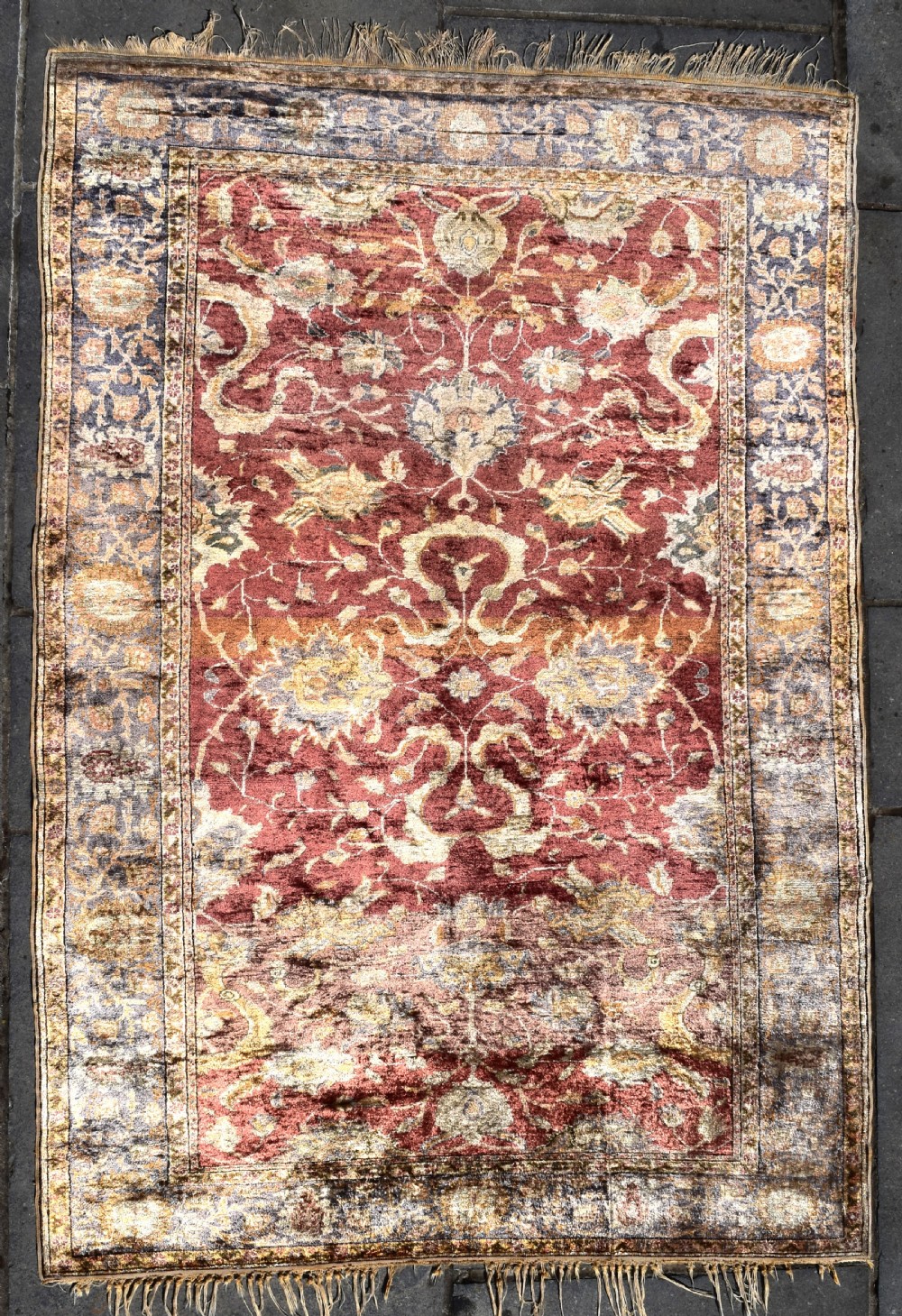 An antique rectangular Turkish Kayseri silk rug featuring an intricate floral central field in red and gold framed by a slate grey border with fringe along the ends.