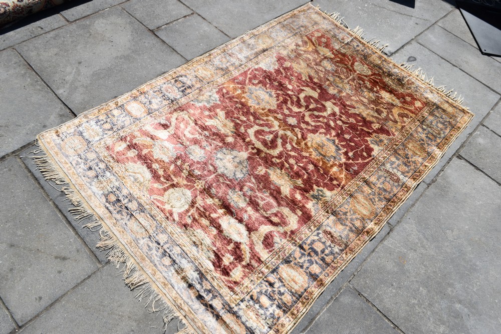 An antique rectangular Turkish Kayseri silk rug featuring an intricate floral central field in red and gold framed by a slate grey border with fringe along the ends. View II