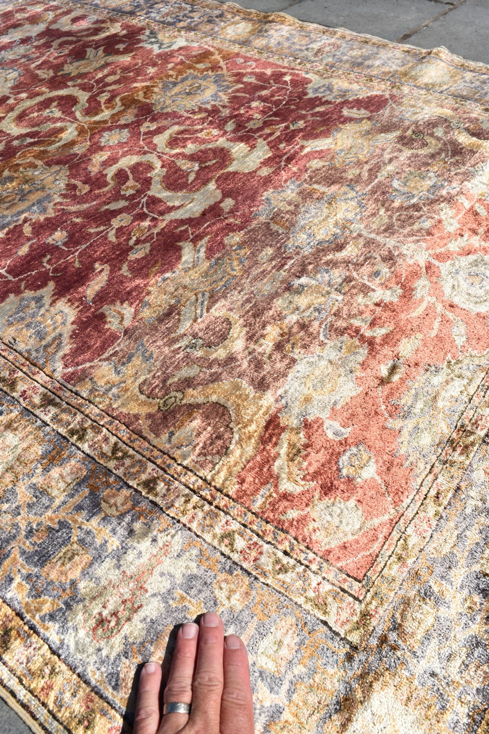 An antique rectangular Turkish Kayseri silk rug featuring an intricate floral central field in red and gold framed by a slate grey border with fringe along the ends. View V