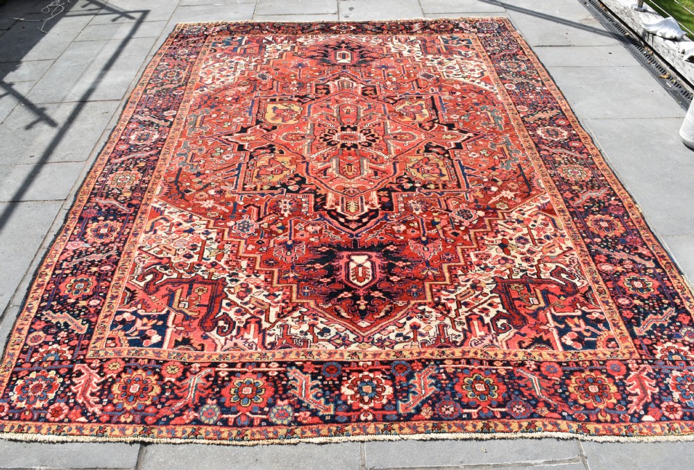 An antique hand-knotted Heriz wool rug featuring a large geometric central medallion in navy and ivory surrounded by a terracotta red field and patterned borders.