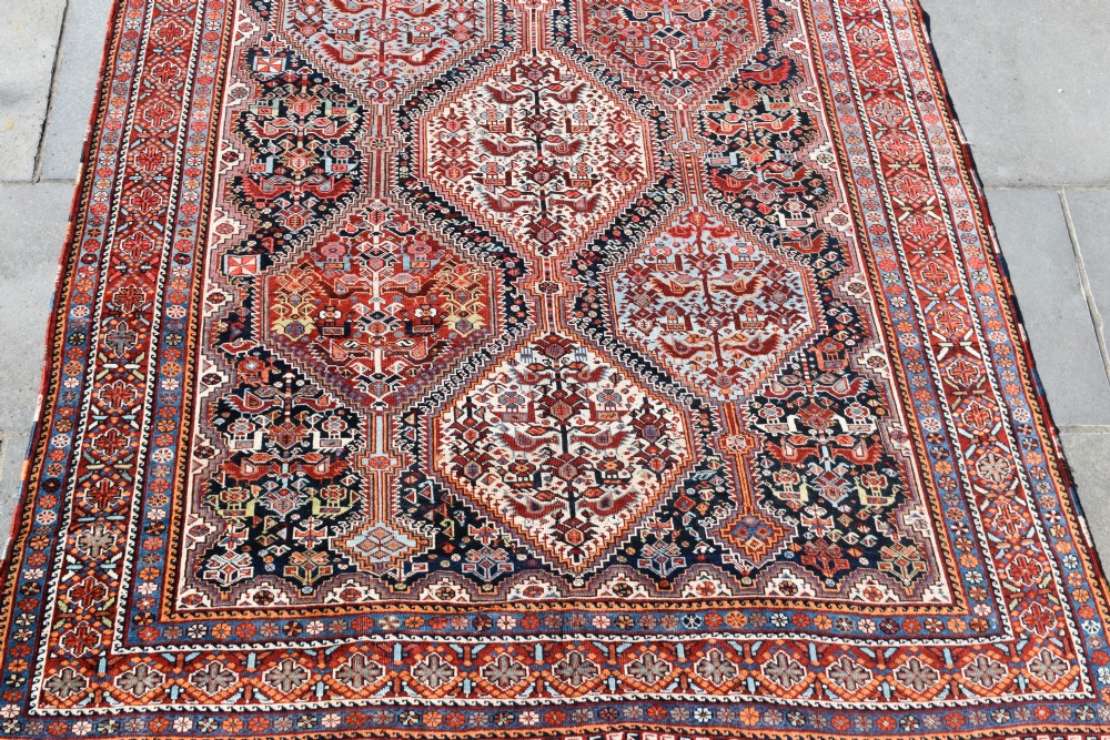 A large hand-knotted wool carpet featuring red, navy, and cream diamond medallions containing stylized bird motifs framed by intricate geometric borders.