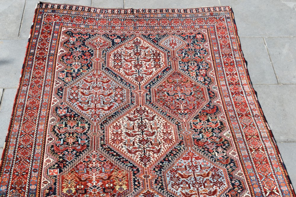A large hand-knotted wool carpet featuring red, navy, and cream diamond medallions containing stylized bird motifs framed by intricate geometric borders. View III