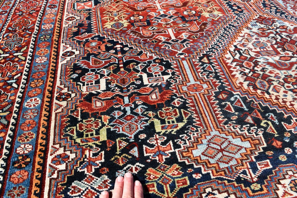 A large hand-knotted wool carpet featuring red, navy, and cream diamond medallions containing stylized bird motifs framed by intricate geometric borders. View IV