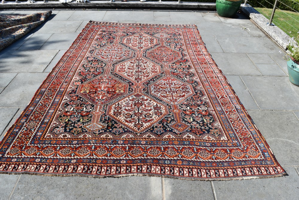 A large hand-knotted wool carpet featuring red, navy, and cream diamond medallions containing stylized bird motifs framed by intricate geometric borders. View V