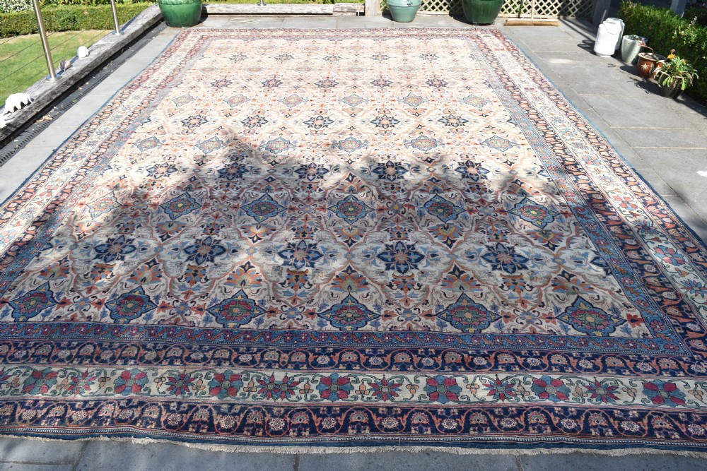 An oversized antique Kirman wool carpet featuring a cream field with intricate floral lattice motifs and a wide navy blue decorative border. View II
