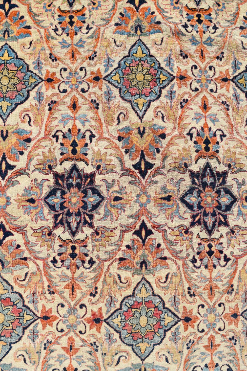 An oversized antique Kirman wool carpet featuring a cream field with intricate floral lattice motifs and a wide navy blue decorative border. View III