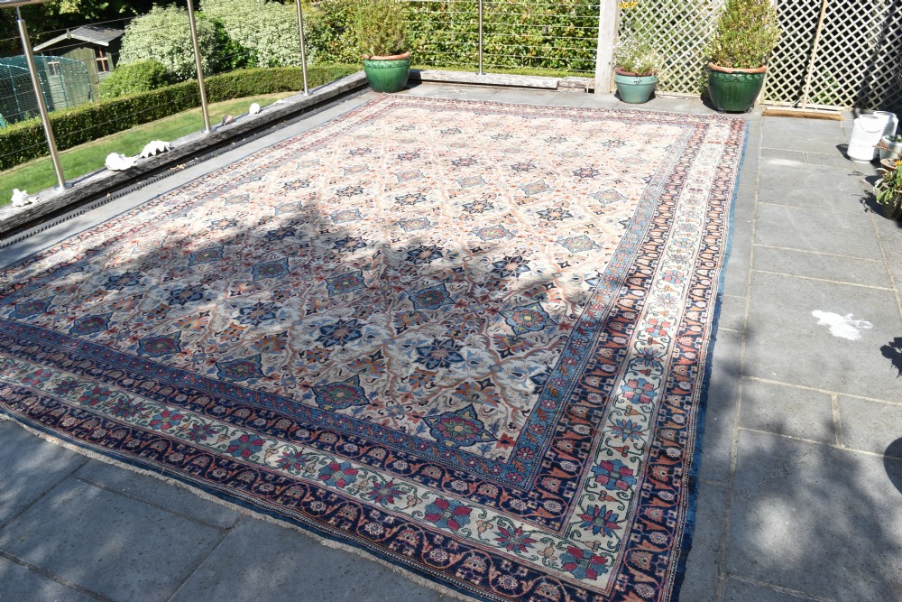 An oversized antique Kirman wool carpet featuring a cream field with intricate floral lattice motifs and a wide navy blue decorative border. View IV