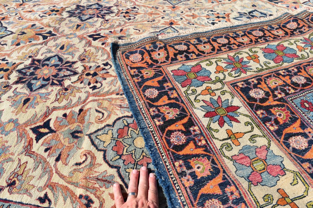 An oversized antique Kirman wool carpet featuring a cream field with intricate floral lattice motifs and a wide navy blue decorative border. View V