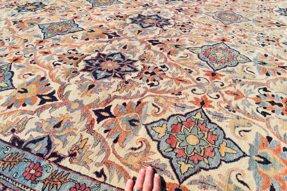 An oversized antique Kirman wool carpet featuring a cream field with intricate floral lattice motifs and a wide navy blue decorative border. View VI