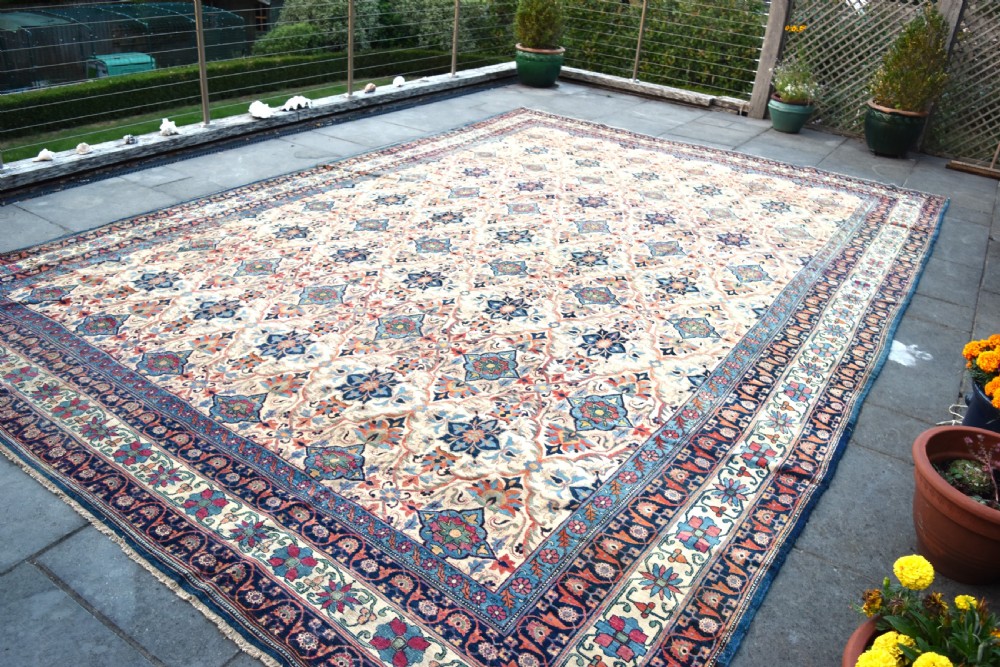 An oversized antique Kirman wool carpet featuring a cream field with intricate floral lattice motifs and a wide navy blue decorative border. View VII