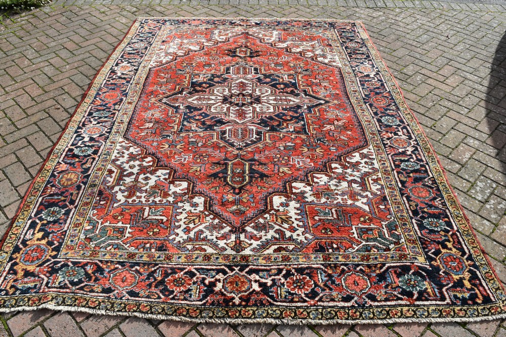 An antique Persian Heriz wool carpet with a bold red and blue central medallion pattern set within a dark decorative border.