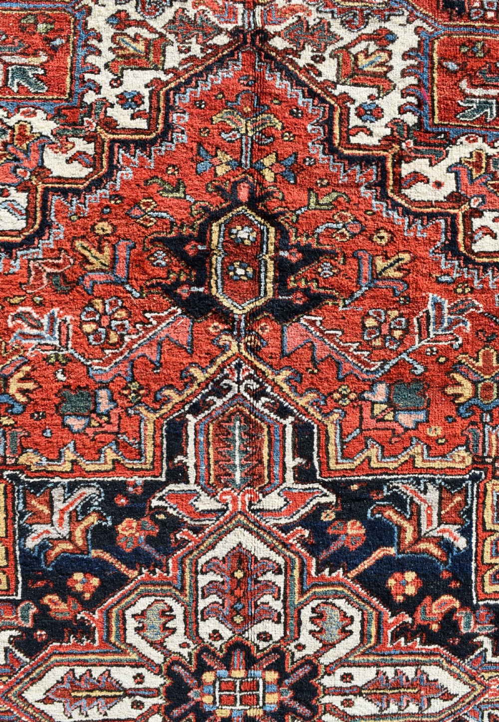 An antique Persian Heriz wool carpet with a bold red and blue central medallion pattern set within a dark decorative border. View II