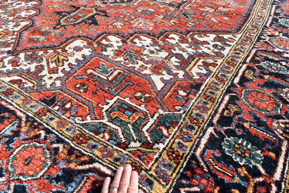 An antique Persian Heriz wool carpet with a bold red and blue central medallion pattern set within a dark decorative border. View III