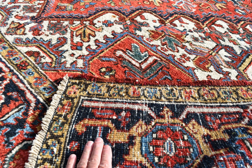An antique Persian Heriz wool carpet with a bold red and blue central medallion pattern set within a dark decorative border. View IV