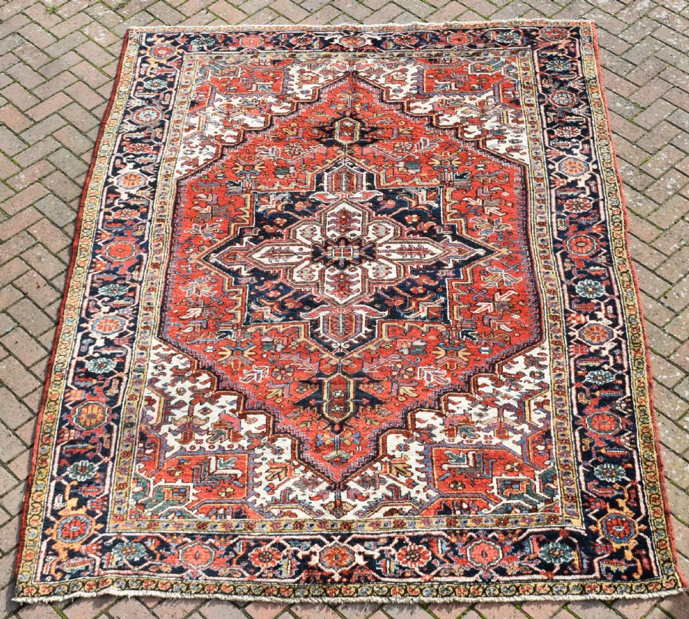 An antique Persian Heriz wool carpet with a bold red and blue central medallion pattern set within a dark decorative border. View V