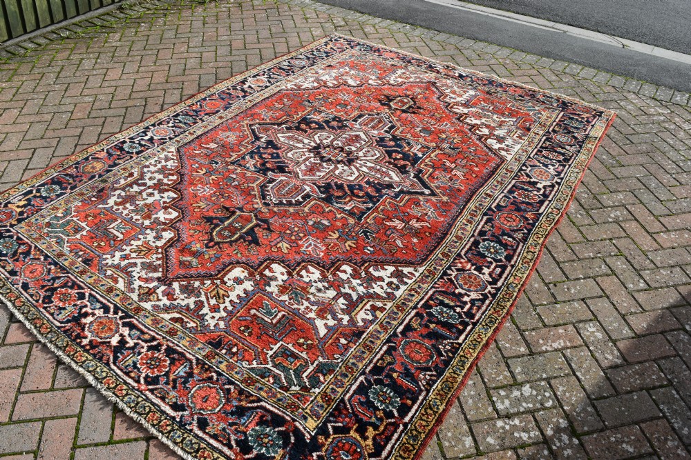 An antique Persian Heriz wool carpet with a bold red and blue central medallion pattern set within a dark decorative border. View VI