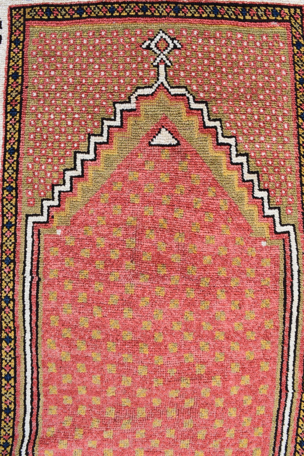 An antique hand-knotted wool Monastir prayer rug featuring a pink and red stepped mihrab arch enclosed by a wide off-white border with colourful rosette motifs. View II