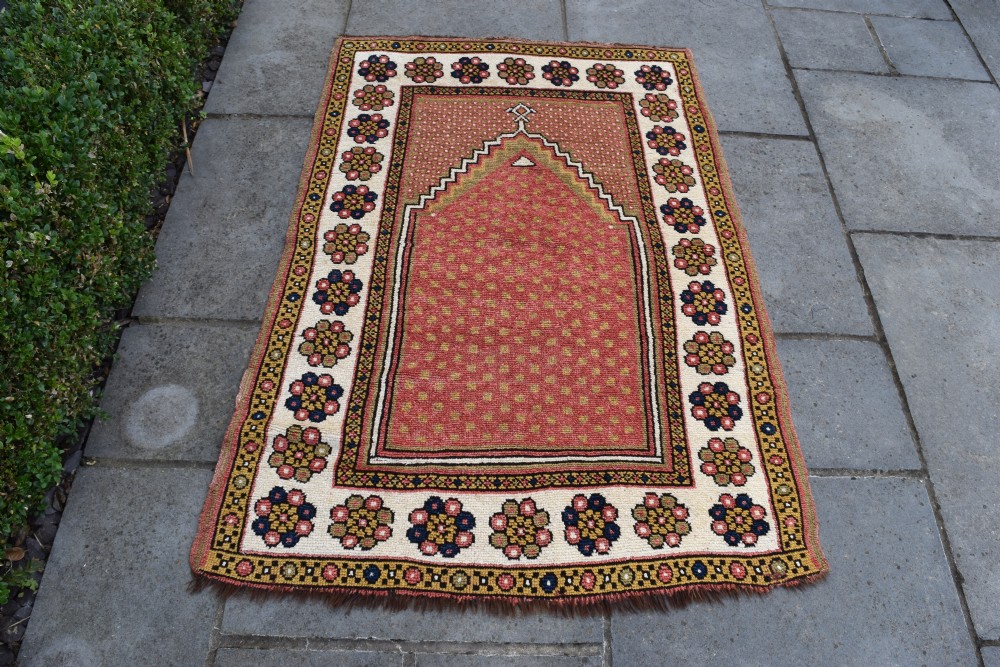 An antique hand-knotted wool Monastir prayer rug featuring a pink and red stepped mihrab arch enclosed by a wide off-white border with colourful rosette motifs. View IV