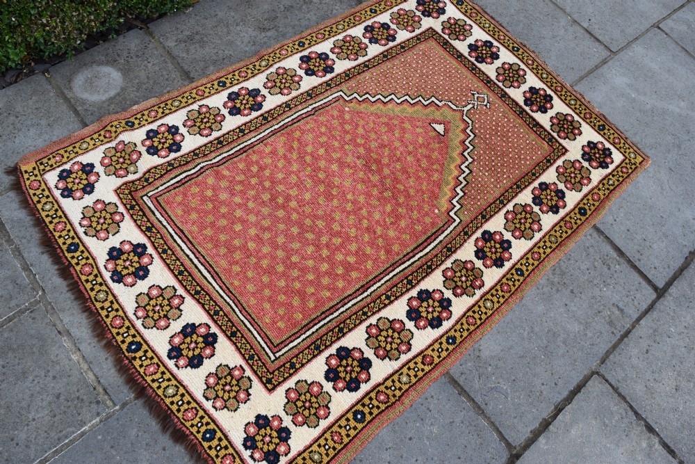 An antique hand-knotted wool Monastir prayer rug featuring a pink and red stepped mihrab arch enclosed by a wide off-white border with colourful rosette motifs. View V