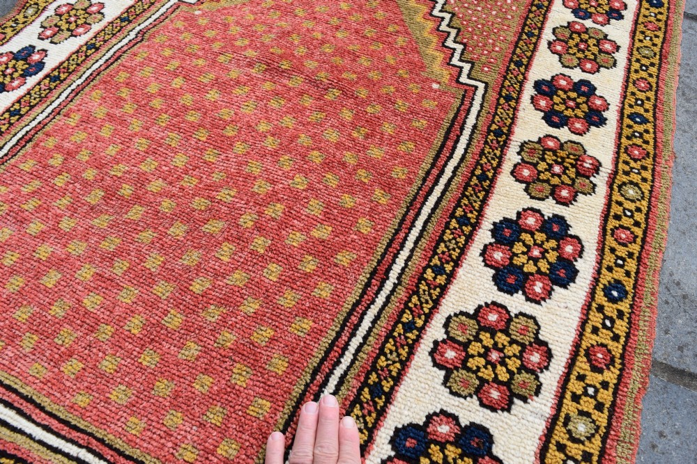 An antique hand-knotted wool Monastir prayer rug featuring a pink and red stepped mihrab arch enclosed by a wide off-white border with colourful rosette motifs. View VI