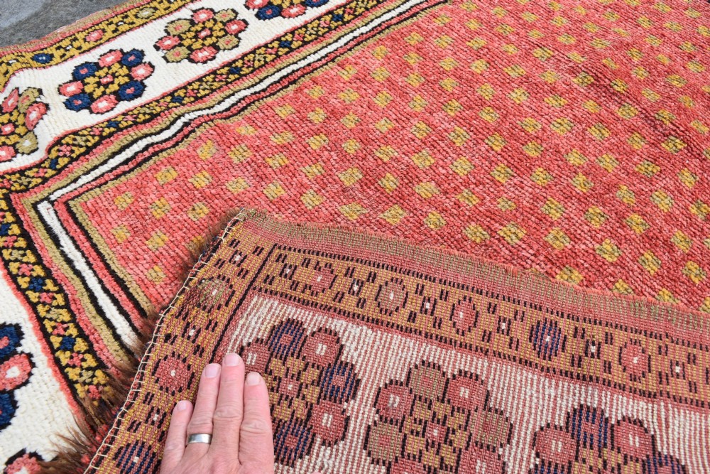 An antique hand-knotted wool Monastir prayer rug featuring a pink and red stepped mihrab arch enclosed by a wide off-white border with colourful rosette motifs. View VII