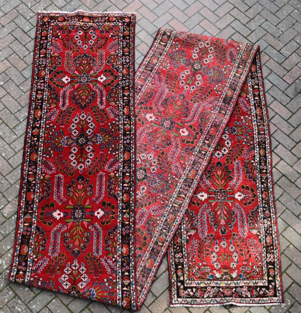 An exceptionally long hand-knotted Persian Sarouk runner rug featuring a deep red ground with detailed floral motifs and a multi-tiered dark border.
