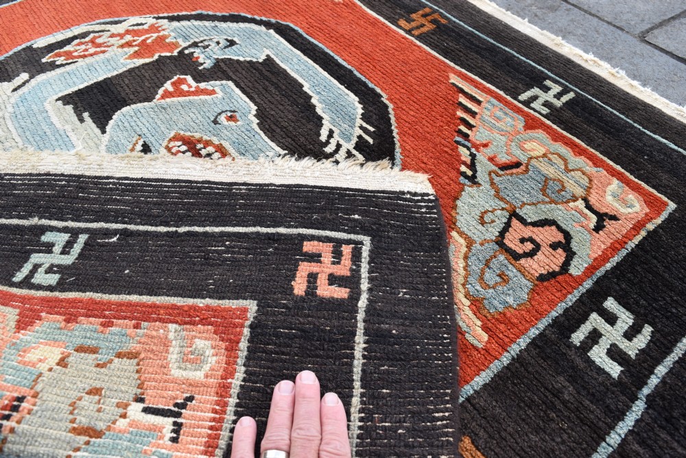 A square hand-knotted Tibetan wool rug featuring a central blue mythical beast inside a circular medallion on a red field with black geometric borders. View III