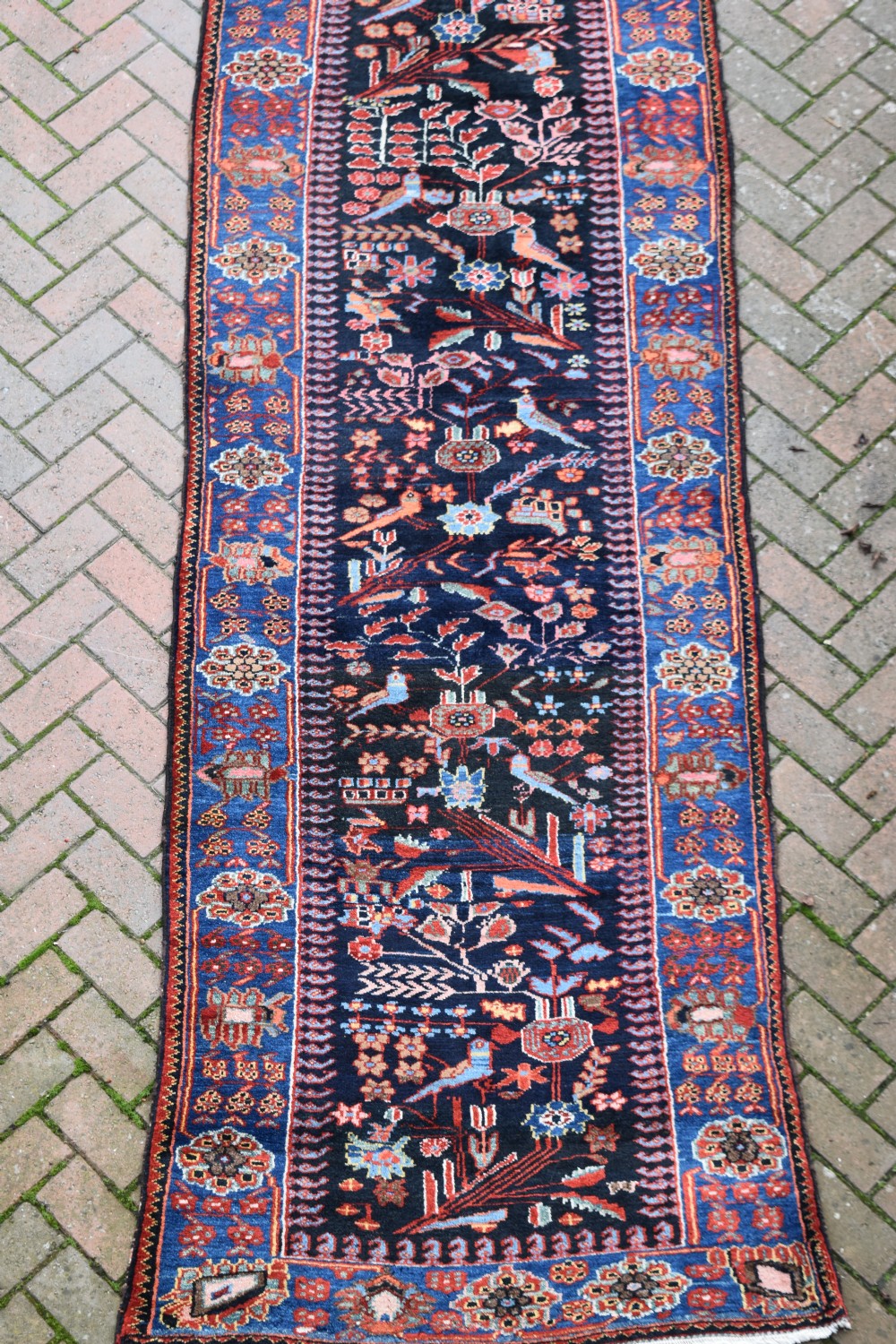 A long, narrow hand-knotted Bakhtiari wool runner rug featuring a navy blue field filled with stylised bird and botanical motifs, enclosed within a bright blue floral border.