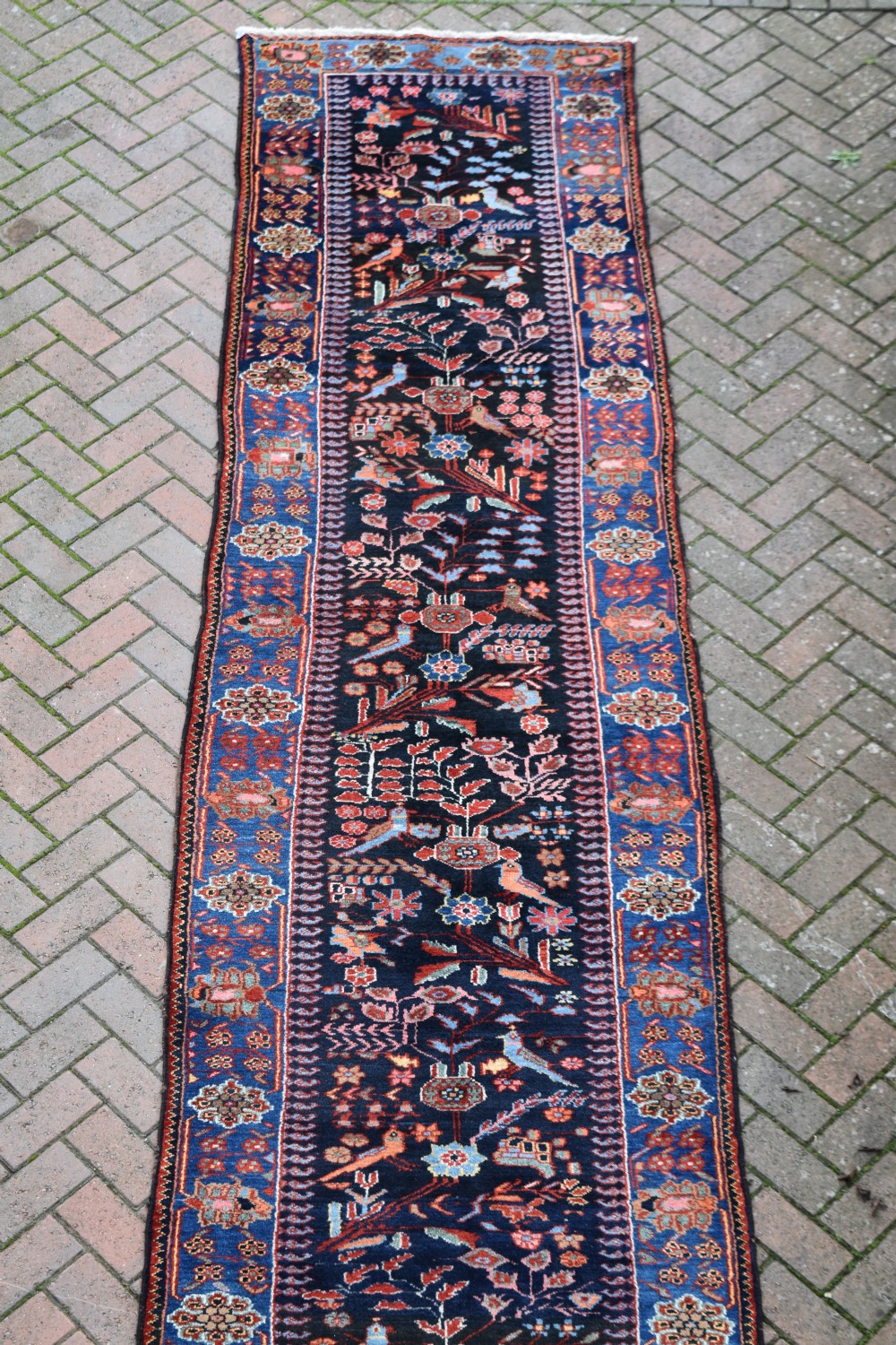 A long, narrow hand-knotted Bakhtiari wool runner rug featuring a navy blue field filled with stylised bird and botanical motifs, enclosed within a bright blue floral border. View III