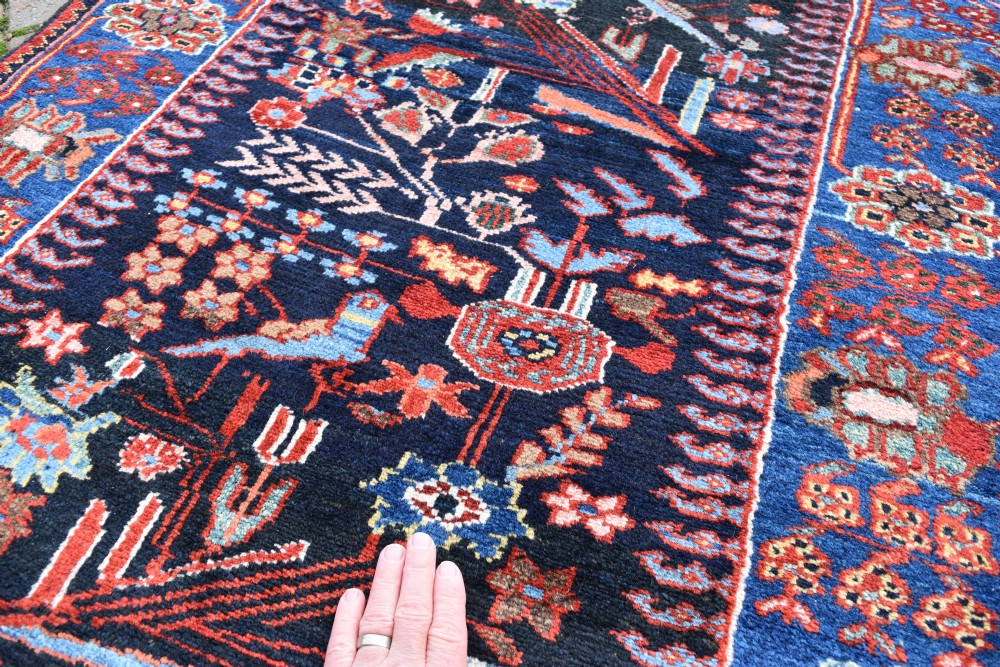 A long, narrow hand-knotted Bakhtiari wool runner rug featuring a navy blue field filled with stylised bird and botanical motifs, enclosed within a bright blue floral border. View IV