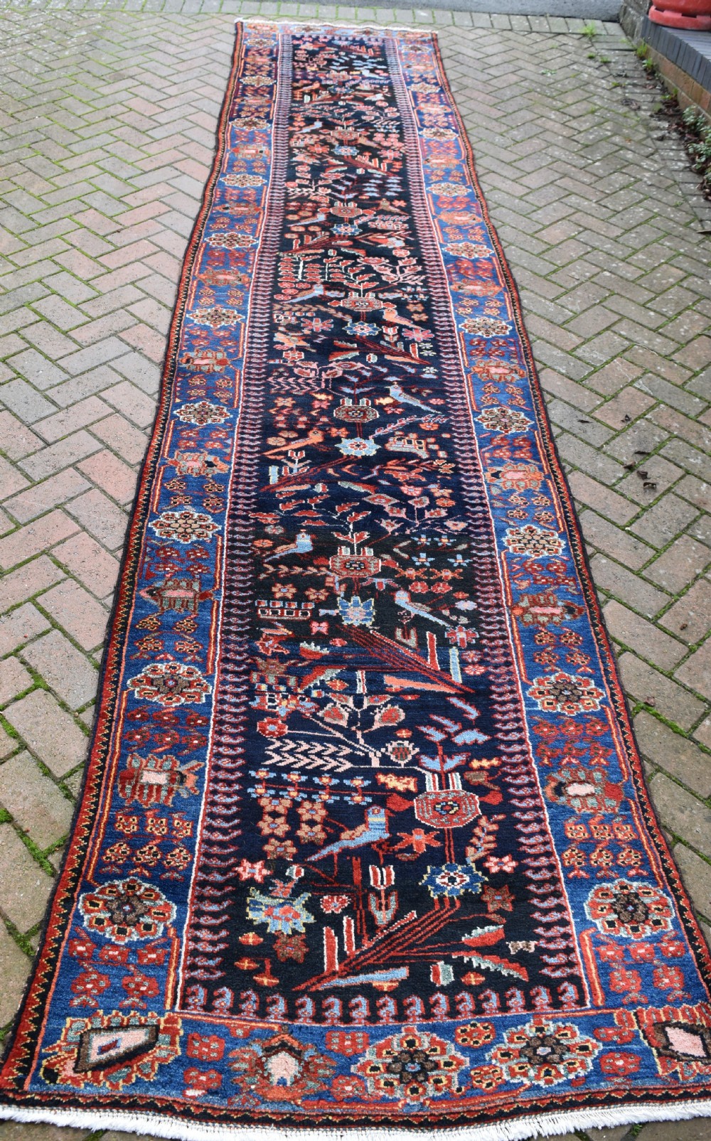 A long, narrow hand-knotted Bakhtiari wool runner rug featuring a navy blue field filled with stylised bird and botanical motifs, enclosed within a bright blue floral border. View VI